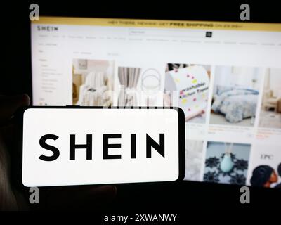Person holding smartphone with logo of fashion e-commerce company Shein in front of website. Focus on phone display. Stock Photo