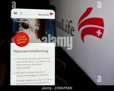 Person holding cellphone with web page of insurance company Swiss Life Holding AG in front of business logo. Focus on center of phone display. Stock Photo