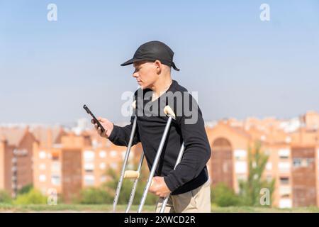 disabled man looking at his smartphone while walking with his crutches Stock Photo