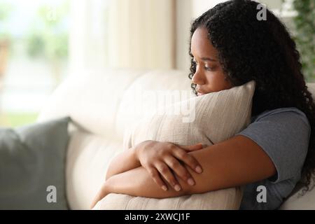 Sad black woman embracing pillow sitting on a couch at home Stock Photo