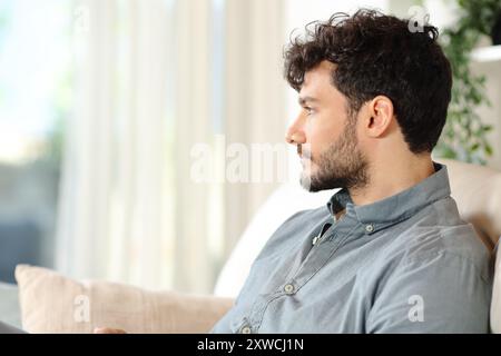 Serious man sitting on a couch looking through a house window Stock Photo