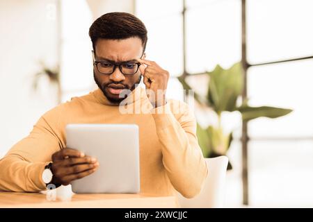 Surprised young afro manager looking at his tablet Stock Photo
