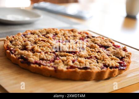 A homemade plum crumble cake on a wooden board in the middle of a dining table. Stock Photo