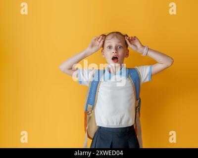 Cute happy kid standing on light yellow background. Child with backpack, little girl is ready to back to school. Stock Photo