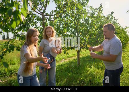 family of four is playing catch bubbles in the garden Stock Photo