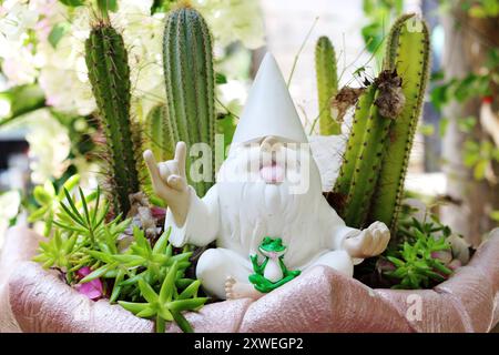 Gnome in cacti planter gives peace and rock vibes. The hand gesture is used to ward off negative energy in Buddhism and for rejuvenation in Hatha yoga Stock Photo