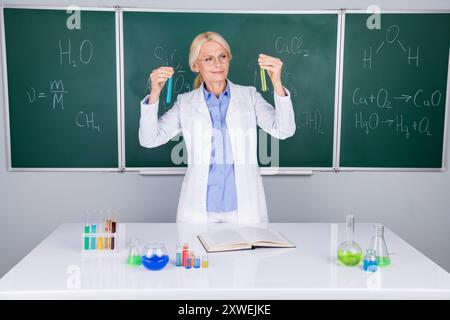 Photo of smart intelligent senior lady wear white coat doing chemical experiment at university isolated on green board background Stock Photo