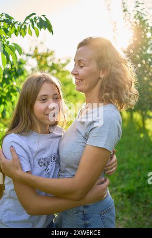 mother and teenage girls with long blond hair spend time together in the sunlit park Stock Photo