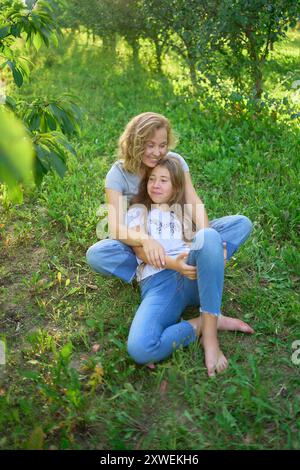 mother and teenage girls with long blond hair spend time together in the sunlit park Stock Photo