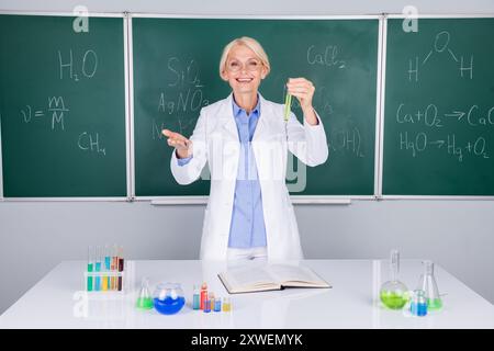 Photo of positive pretty intelligent senior lady wear white coat doing chemical research isolated on green board background Stock Photo