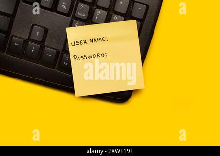 A yellow paper note with user name and password word on a black computer keyboard on a yellow background Stock Photo