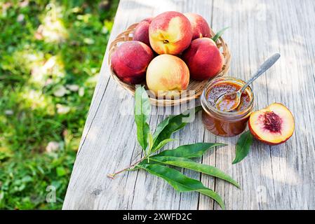 Peach jam or marmalade in a glass jar with ripe peaches, outdoors on sunny day Stock Photo