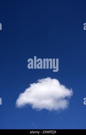Lonely fluffy white cloud in deep blue sky. Clear blue sky in summer apart from almost perfectly formed cumulus cloud Stock Photo