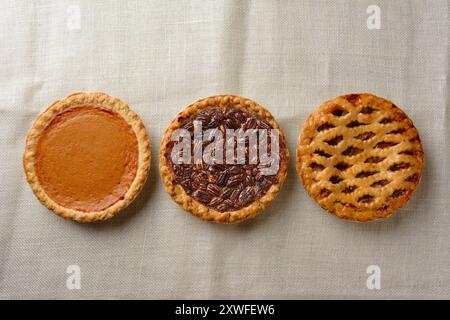 Overhead still life of fresh baked pecan, pumpkin, and apple pies on a burlap table cloth. Stock Photo