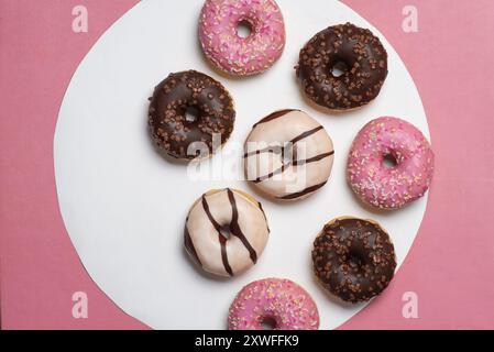 A delightful assortment of donuts with vibrant pink, chocolate, and white icing, paired with sprinkles, showcased on a contrasting white and pink back Stock Photo