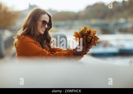 Hello november. smiling elegant female in orange trench coat with autumn yellow leaves in the city. Stock Photo