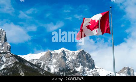 Canadian flag flying on pole against blue sky and mountains Stock Photo