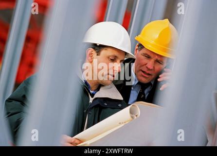 An architect and construction worker reviewing blueprints at a construction site Stock Photo