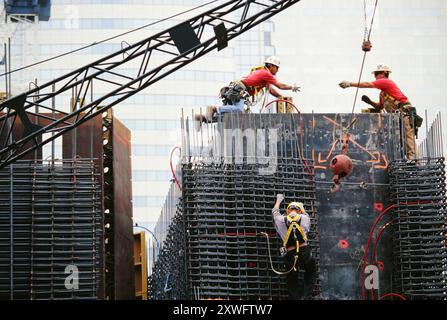 Workers collaborate to lift materials while constructing a large structure on a busy urban construction site. Stock Photo