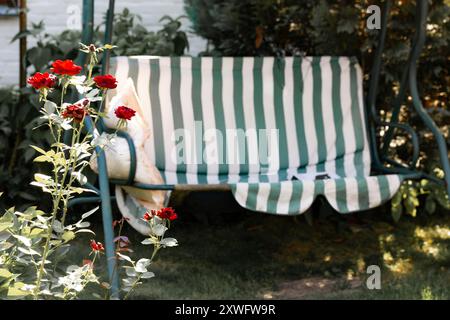 Green white garden swing on a patio backyard in a home garden. A place to relax among blossoming red roses. Rural lifestyle. Place for recreation. Stock Photo