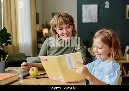 Adorable and smiling daughter showing her brand new painting to her mother while she using tablet Stock Photo