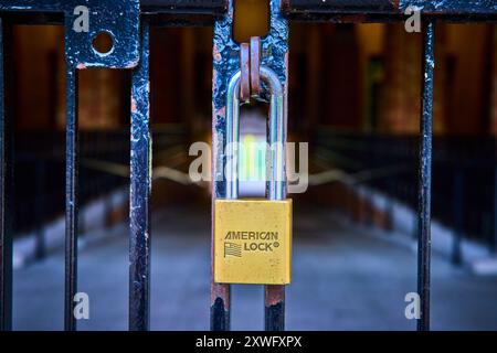 Close-Up Yellow Padlock on Rusty Gate with Blurred Passageway Background Stock Photo