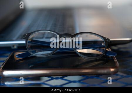 A laptop and a cell phone and glasses are placed on a table Stock Photo
