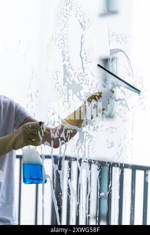 a man in a white shirt and yellow protective  gloves is cleaning a window Stock Photo