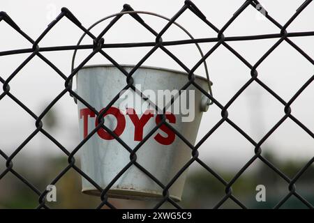 silver toy bucket with red lettering hanging from fence Stock Photo