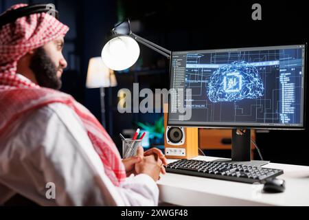 Detailed image of Middle Eastern developer in front of desktop pc monitoring a complex network, ensuring data security and efficient computing using cloud, AI, and machine learning. Stock Photo