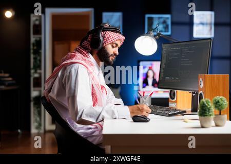 Middle Eastern software developer demonstrating the fundamentals of software development by entering code on a laptop. Arab man running algorithms while using wireless headphones. Stock Photo