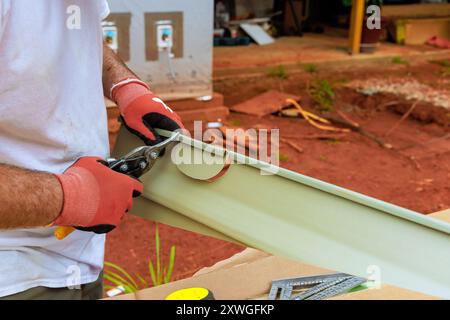 Before installing plastic vinyl siding, worker uses of scissors to cut it to size Stock Photo