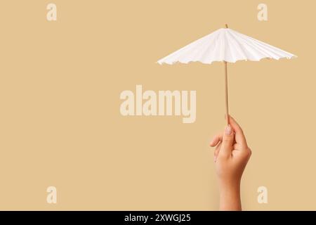 Female hand with mini umbrella on beige background Stock Photo