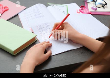 Woman writing math formulas in copybook at dark table Stock Photo
