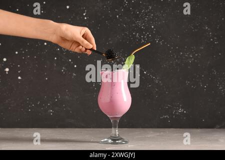 Female hand with blackberry and glass of fresh smoothie on grey table Stock Photo