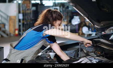 Precise mechanic in garage using torque wrench to tighten screws inside opened up vehicle after changing oil. Auto repair shop employee doing checkup on car, cleaning leftover mess Stock Photo