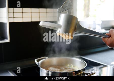Spaetzle dough is pressed through a spaetzle press Stock Photo