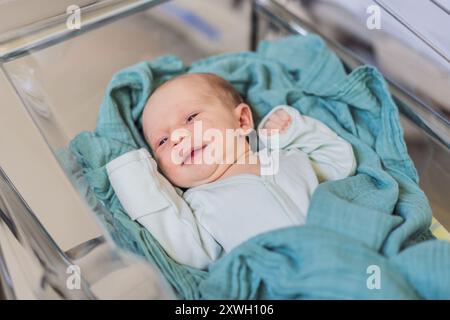 A newborn rests peacefully in his transparent bassinet in the hospital. The clear bassinet provides visibility for medical staff to monitor the baby's Stock Photo