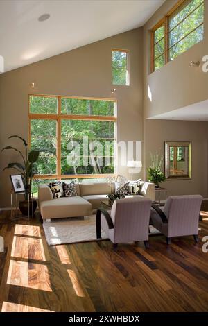 Corner of living room with large windows at multiple levels looking out to lots of green trees Stock Photo