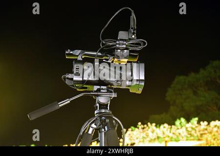 Tripod mounted video camera, Side view of modern 4K broadcast cameras on a tripod, wedding ceremony, night scene. Stock Photo