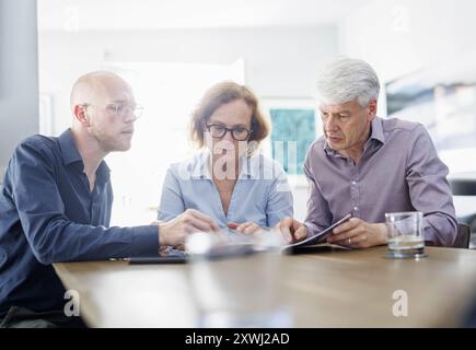 Symbolfoto zum Thema Beratung. Eine aeltere Frau und ein aelterer Mann sitzen zu Hause zusammen an einem Tisch und werden von einem jungen Mann berate Stock Photo