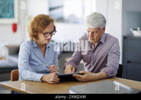 Symbolfoto. Eine Frau und ein Mann sitzen zusammen an einem Tisch mit einem Tablet und unterhalten sich. Berlin, 13.08.2024. Berlin Deutschland *** Sy Stock Photo