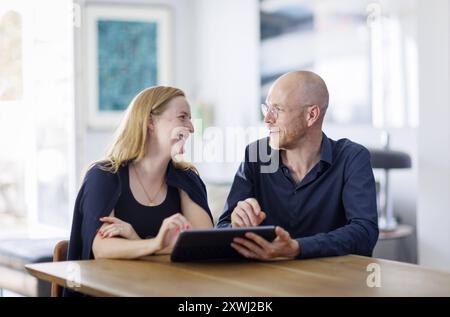 Symbolfoto. Eine Frau und ein Mann sitzen zusammen an einem Tisch mit einem Tablet und unterhalten sich. Berlin, 13.08.2024. Berlin Deutschland *** Sy Stock Photo