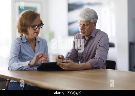 Symbolfoto. Eine Frau und ein Mann sitzen zusammen an einem Tisch mit einem Tablet und unterhalten sich. Berlin, 13.08.2024. Berlin Deutschland *** Sy Stock Photo