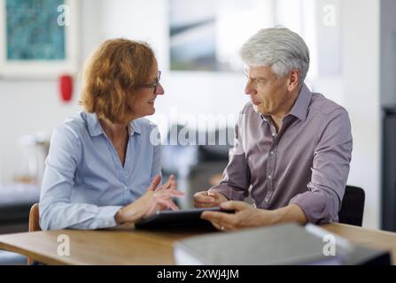 Symbolfoto. Eine Frau und ein Mann sitzen zusammen an einem Tisch mit einem Tablet und unterhalten sich. Berlin, 13.08.2024. Berlin Deutschland *** Sy Stock Photo