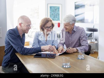 Symbolfoto zum Thema Beratung. Eine aeltere Frau und ein aelterer Mann sitzen zu Hause zusammen an einem Tisch und werden von einem jungen Mann berate Stock Photo