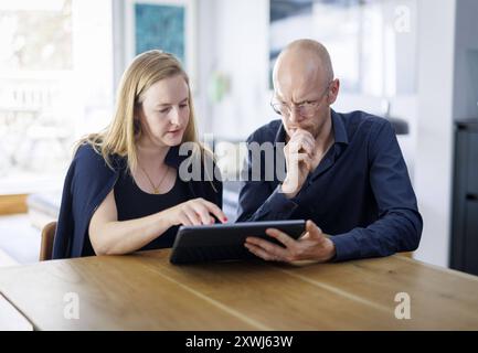 Symbolfoto. Eine Frau und ein Mann sitzen zusammen an einem Tisch mit einem Tablet und unterhalten sich. Berlin, 13.08.2024. Berlin Deutschland *** Sy Stock Photo