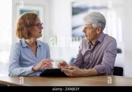 Symbolfoto. Eine Frau und ein Mann sitzen zusammen an einem Tisch mit einem Tablet und unterhalten sich. Berlin, 13.08.2024. Berlin Deutschland *** Sy Stock Photo