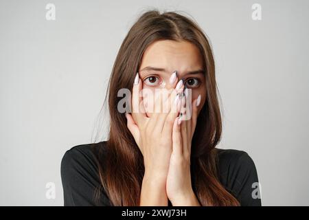 Young Woman Covering Her Face With Hands While Looking Scared Stock Photo