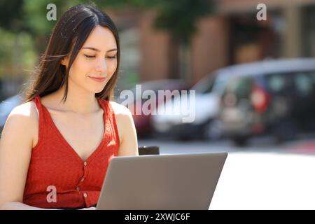 Asian woman using laptop sitting on a bench in the street Stock Photo